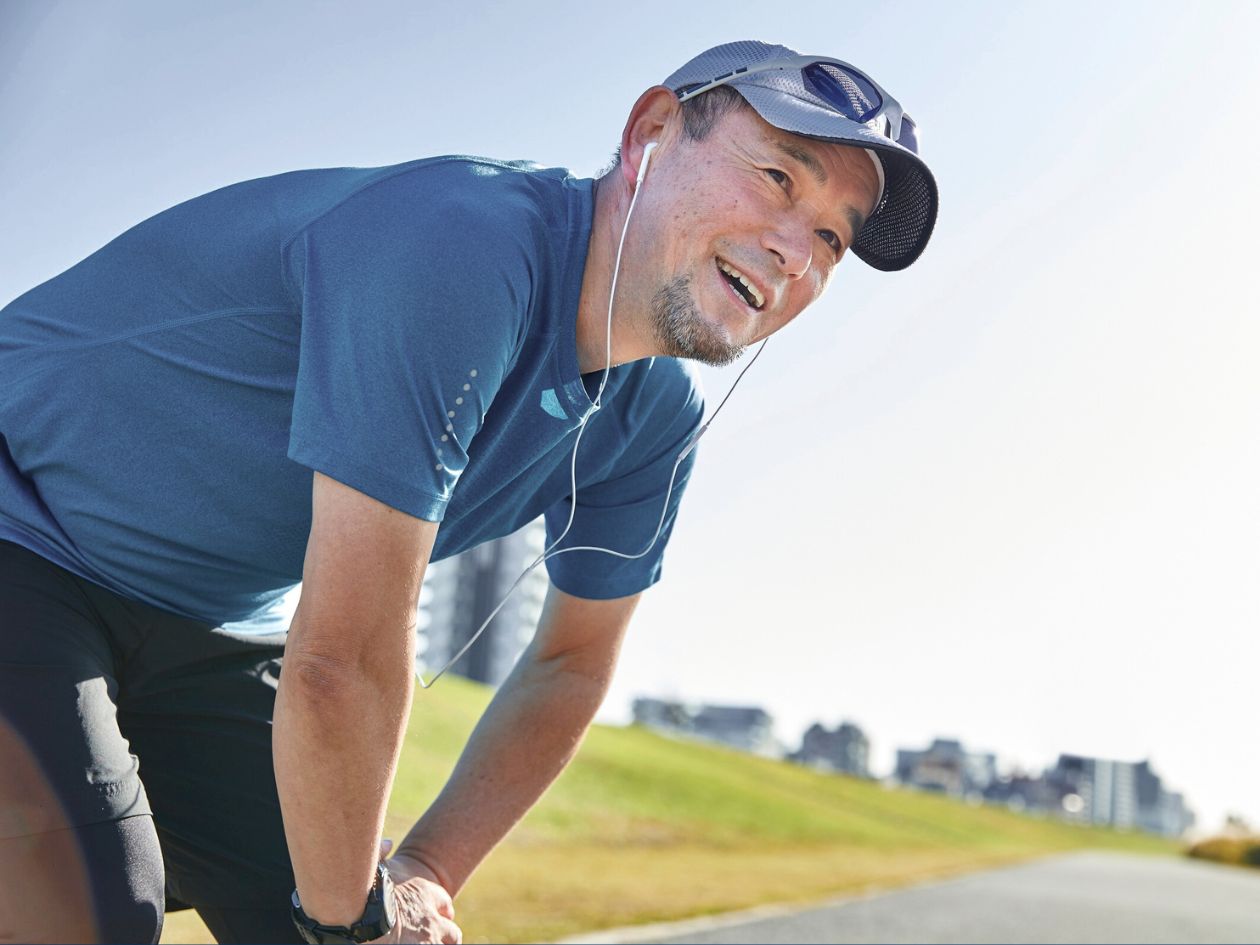 Photo of a smiling man outdoors in workout gear, bent over with his hands on his left knee, as if he's resting during a run