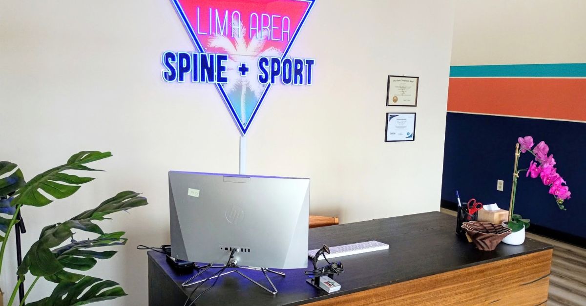 Front desk and check-in area at Lima Area Spine + Sport, with the clinic's neon sign above the reception desk.