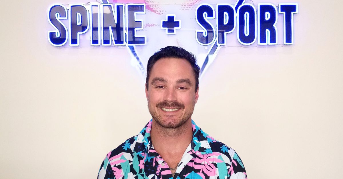 Dr. Kevin Pisle smiling beneath the Spine + Sport neon sign at the Lima, Ohio clinic.