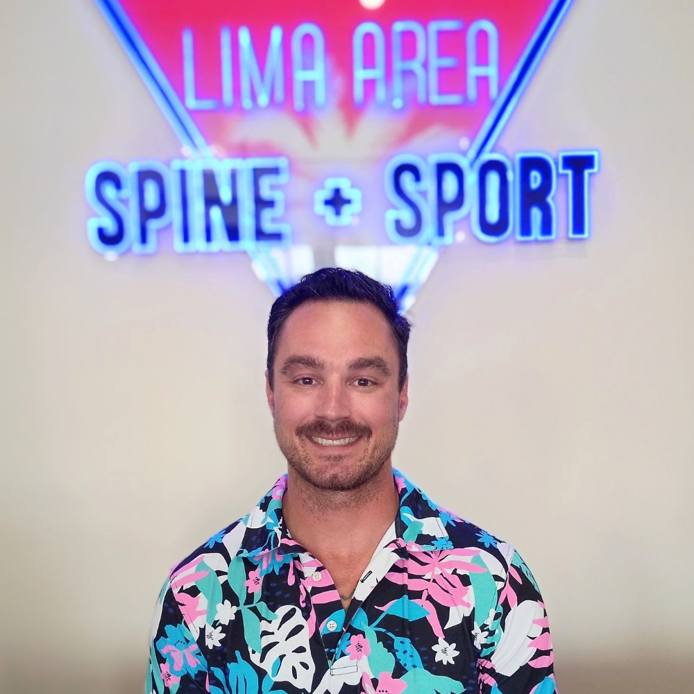Dr. Kevin Pisle standing beneath the Lima Area Spine + Sport neon sign in the Lima, OH clinic.