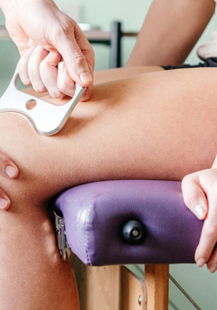 Up close photo of instrument assisted soft tissue mobilization (IASTM) with a stainless steel tool on a woman's upper leg